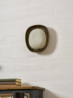 This Clérachic wall light, switched off, shows a frosted white shade inside a rounded bronze rim, on a textured pale wall.