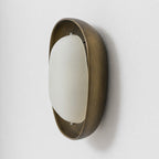 This Clérachic wall light is seen from a steep side angle, showing the depth of the bronze bowl and the curve of the frosted shade.