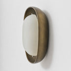 Side view of this Clérachic wall light, with a brushed bronze bowl and a smooth, pale frosted shade set slightly forward.
