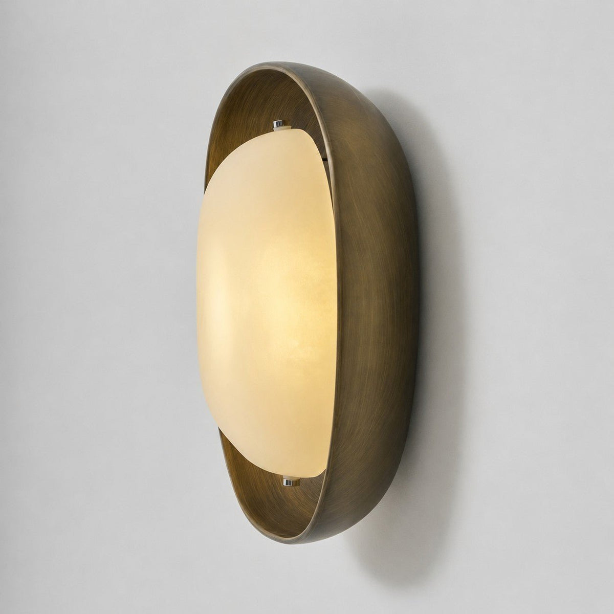 The frosted shade of this Clérachic wall light glows warm in a deep bronze bowl, seen from the side on a pale grey backdrop.