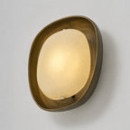 A lit Clérachic wall light, angled slightly, with a warm glow across the frosted shade and a brushed bronze rim around it.
