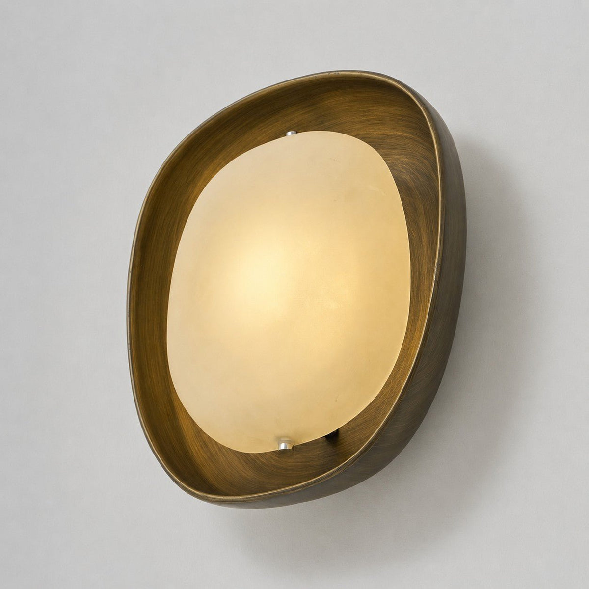 A lit Clérachic wall light, angled slightly, with a warm glow across the frosted shade and a brushed bronze rim around it.