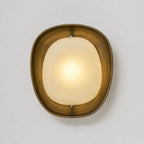 Front view of this Clérachic wall light lit warm, with the brushed bronze inner rim catching the glow from the frosted shade.