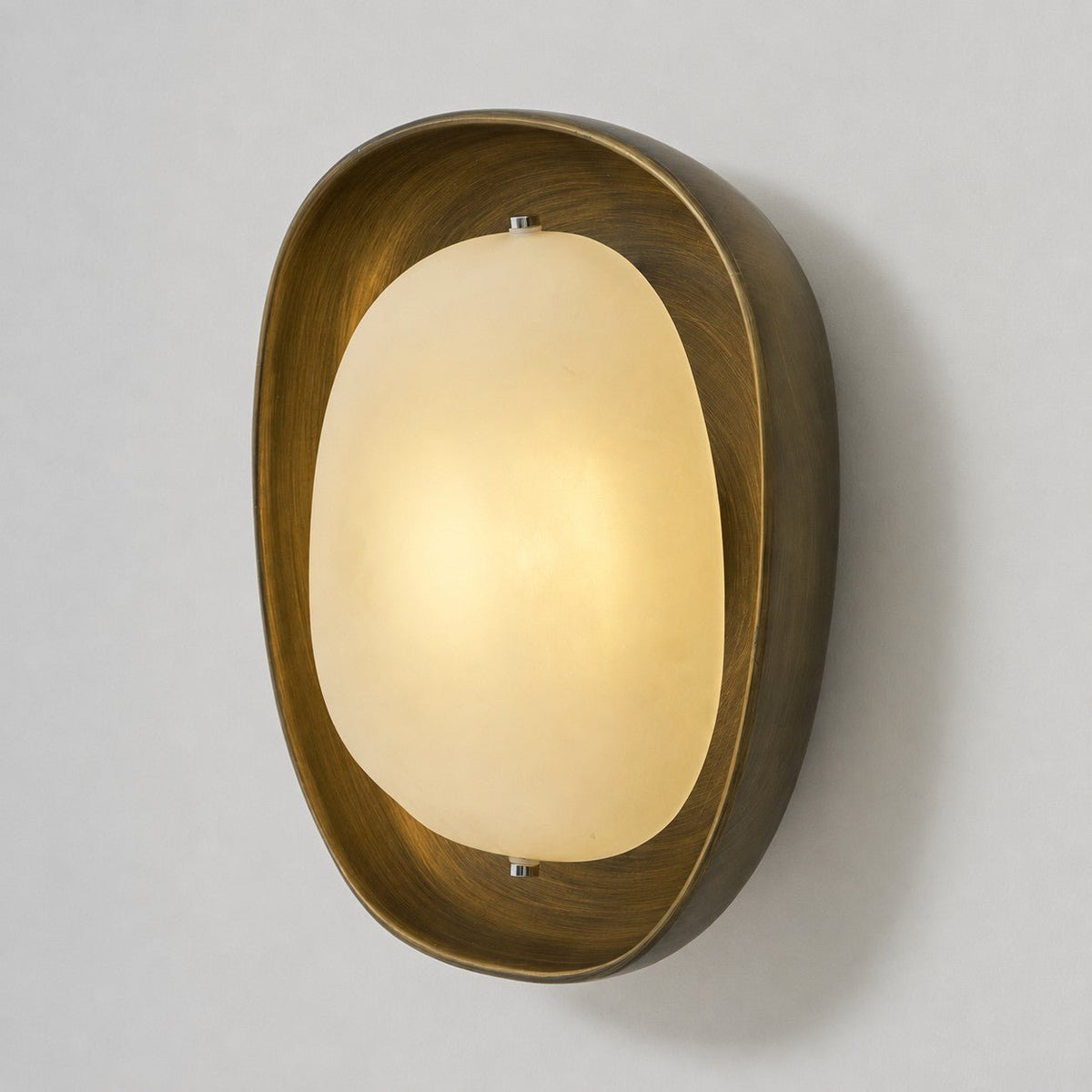 Seen from a slight angle, a lit Clérachic wall light glows warm in its bronze bowl on a plain grey wall.