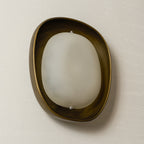 A Clérachic wall light switched off and turned slightly, with soft cloudy glass inside a bronze rim, on a cream wall.