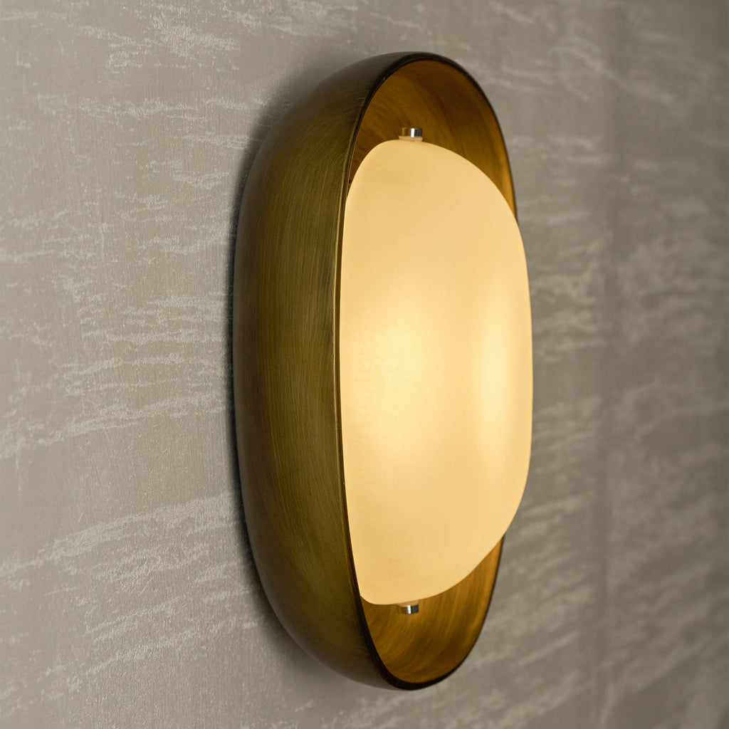 Seen from the side, a lit Clérachic wall light glows gold in its bronze bowl against a pale, streaked plaster wall.