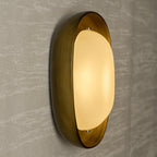 Seen from the side, a lit Clérachic wall light glows gold in its bronze bowl against a pale, streaked plaster wall.
