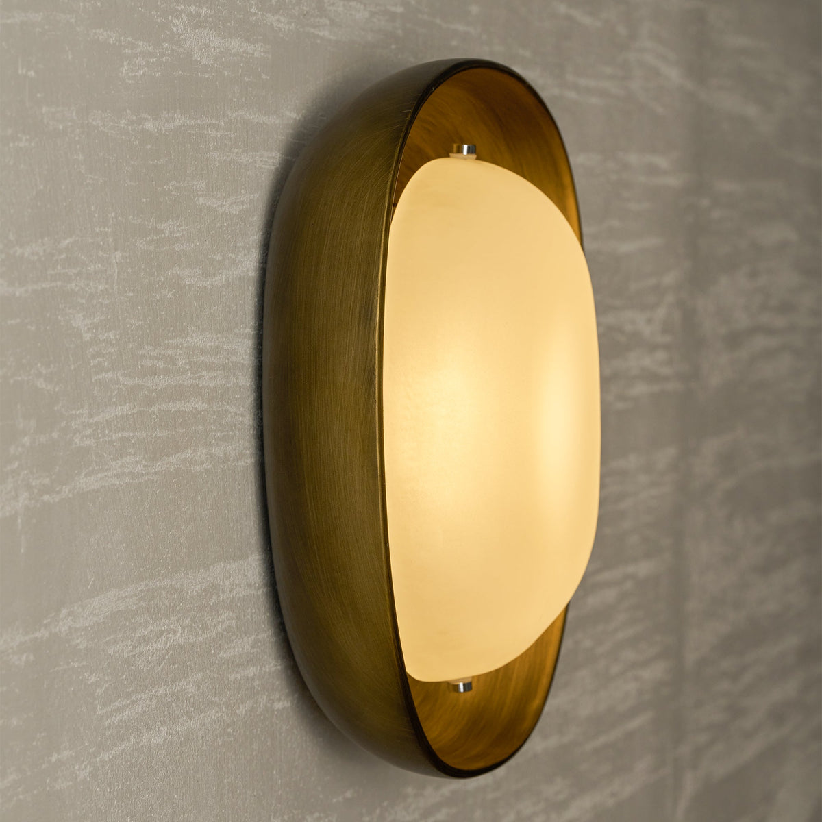 Seen from the side, a lit Clérachic wall light glows gold in its bronze bowl against a pale, streaked plaster wall.