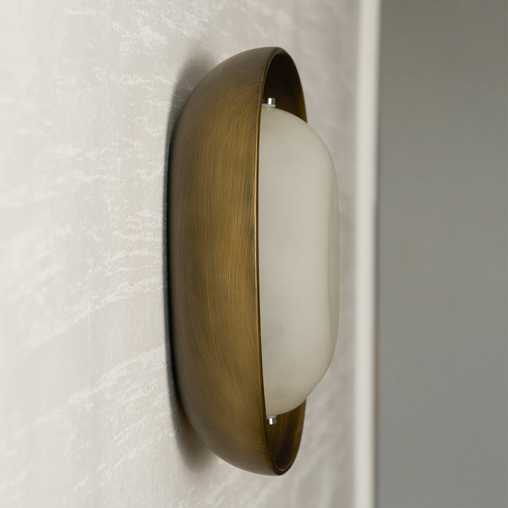 Side-on view of a Clérachic wall light switched off, with a bronze bowl and a milky white frosted shade, on a pale wall.