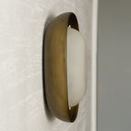 Side-on view of a Clérachic wall light switched off, with a bronze bowl and a milky white frosted shade, on a pale wall.