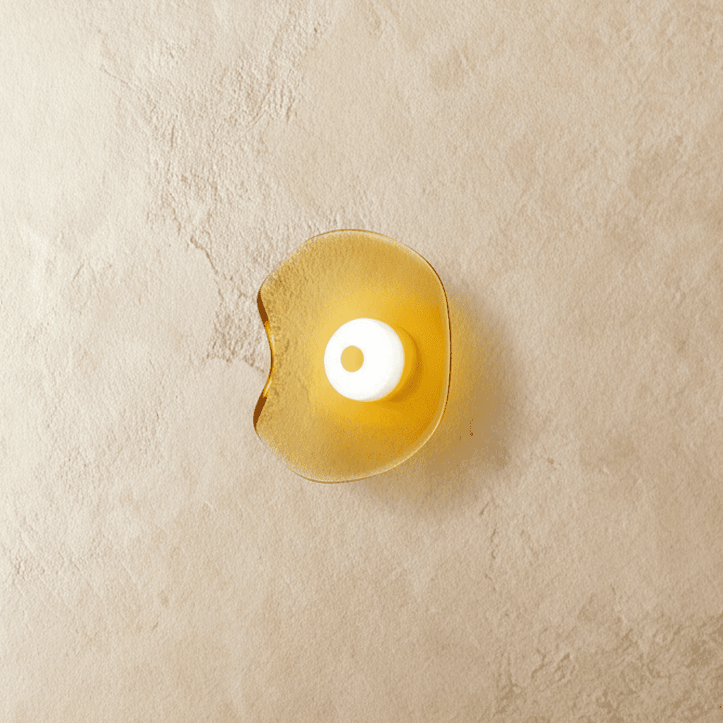 Clérachic wall light with a rippled, free-form amber glass shade and a white glass centre disc, glowing on limewash.