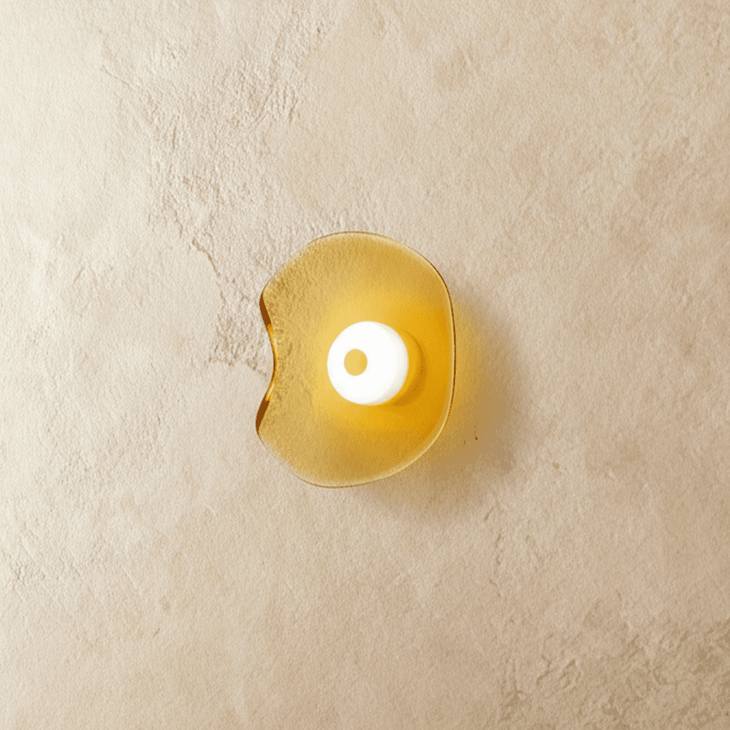 Clérachic wall light with a rippled, free-form amber glass shade and a white glass centre disc, glowing on limewash.