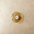 Clérachic wall light with a free-form amber glass shade and a cream glass centre disc, shown switched off on limewash.