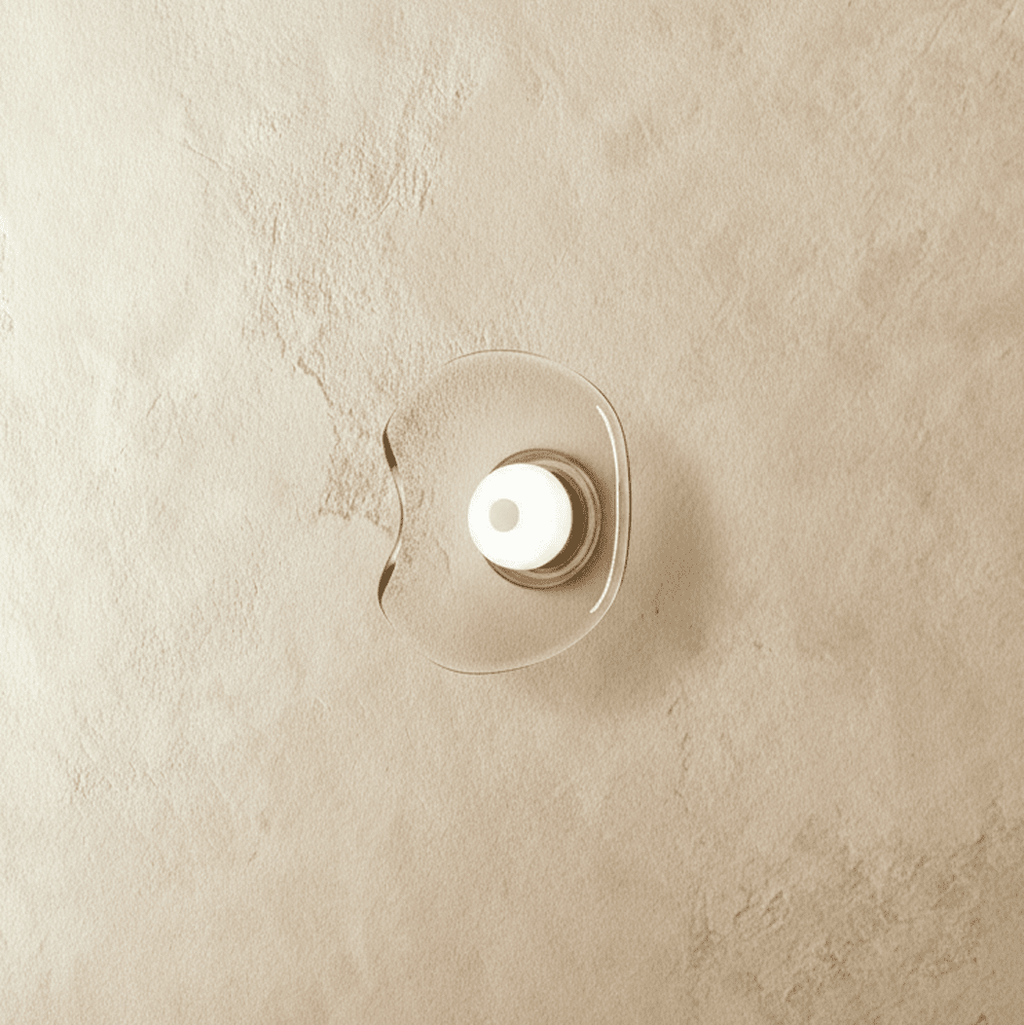Clérachic wall light with a free-form clear glass shade and a white glass centre disc, switched off on a limewashed wall.