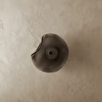 Clérachic wall light with a free-form smoky grey glass shade and a dark centre disc, switched off on limewash.