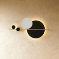 Clérachic wall lamp of overlapping black and white flat discs on a thin brass bar, with a warm glow behind the large black disc.