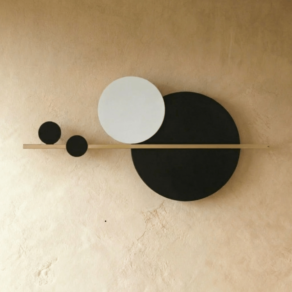 Clérachic black and white disc wall lamp on a slim brass bar, shown unlit on a limewash wall.