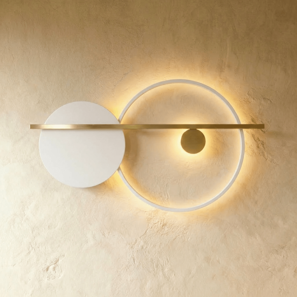Clérachic white ring wall lamp with a white disc and a brass bar, its ring edge-lit with a warm glow on a limewash wall.