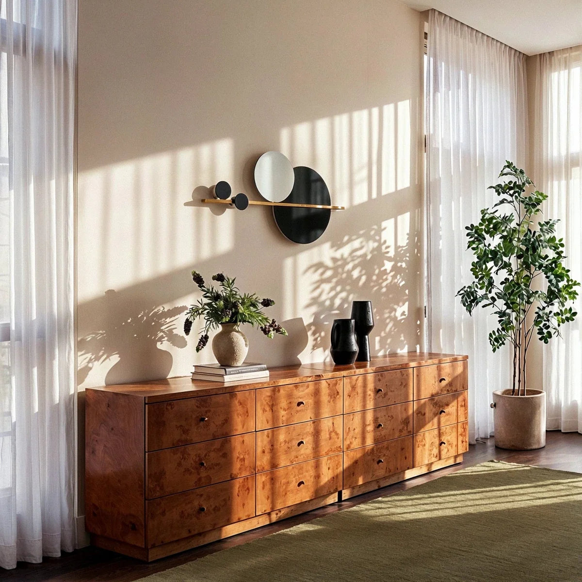 Clérachic black and white disc wall lamp on a brass bar, hung above a burr-wood chest of drawers beside sheer curtains.