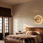 Clérachic white ring wall lamp with a brass bar, glowing warm above a bed with a tartan throw in a calm bedroom.