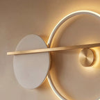 Clérachic close view of a white disc and glowing white ring wall lamp, with a brushed brass bar and small brass disc.