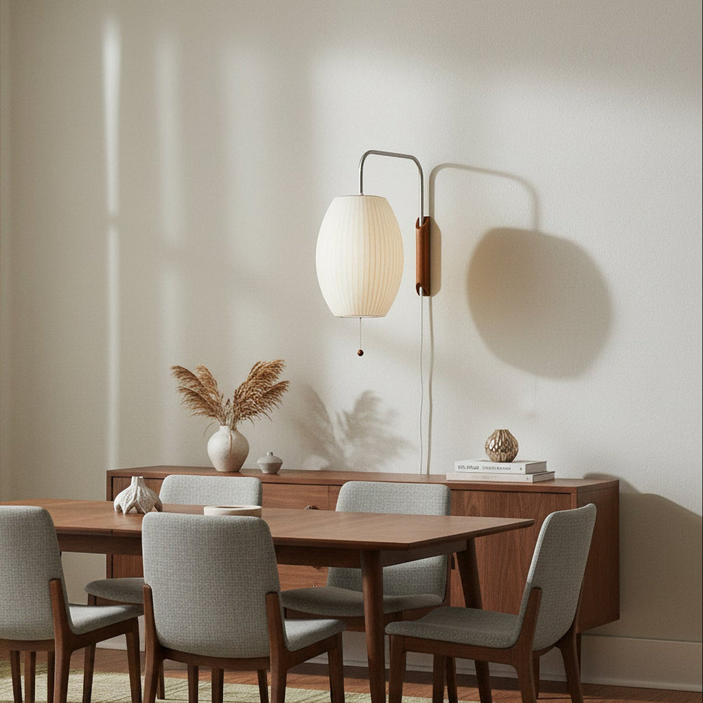 A Clérachic plug-in wall light with an oval white shade hangs above a walnut sideboard and dining table, its pull cord and white cable running down the wall.