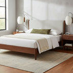 Two matching Clérachic wall lights flank a bed with a pale upholstered headboard and walnut frame, one oval shade at each side.