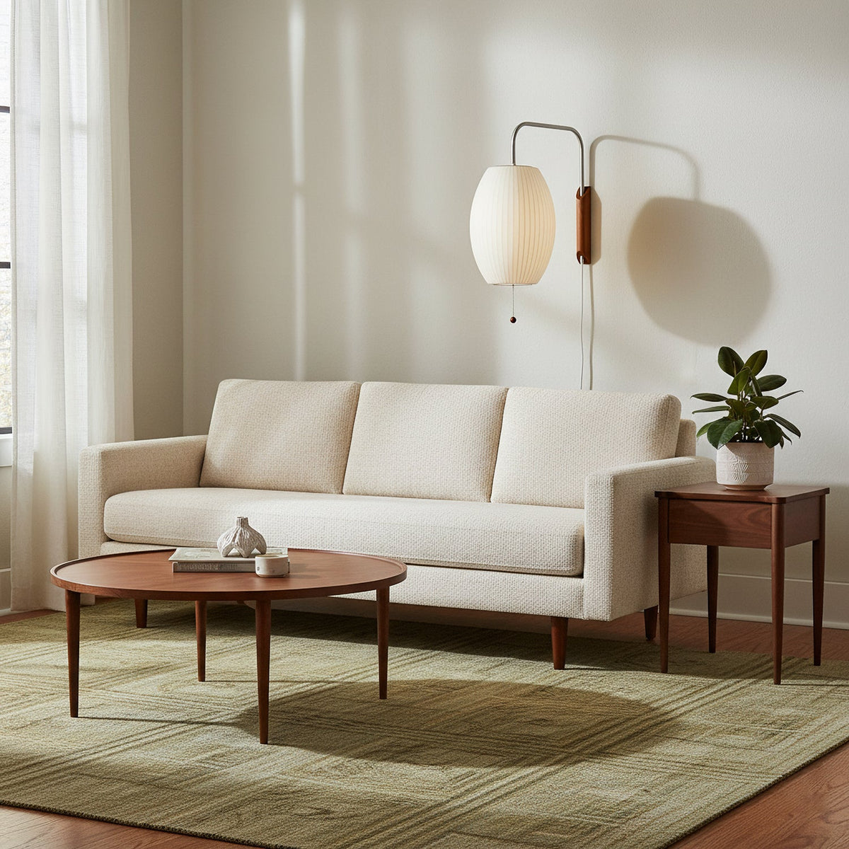 Oval shade of a Clérachic plug-in sconce casts a soft shadow on a cream wall above a pale sofa, a round walnut coffee table and a potted plant.