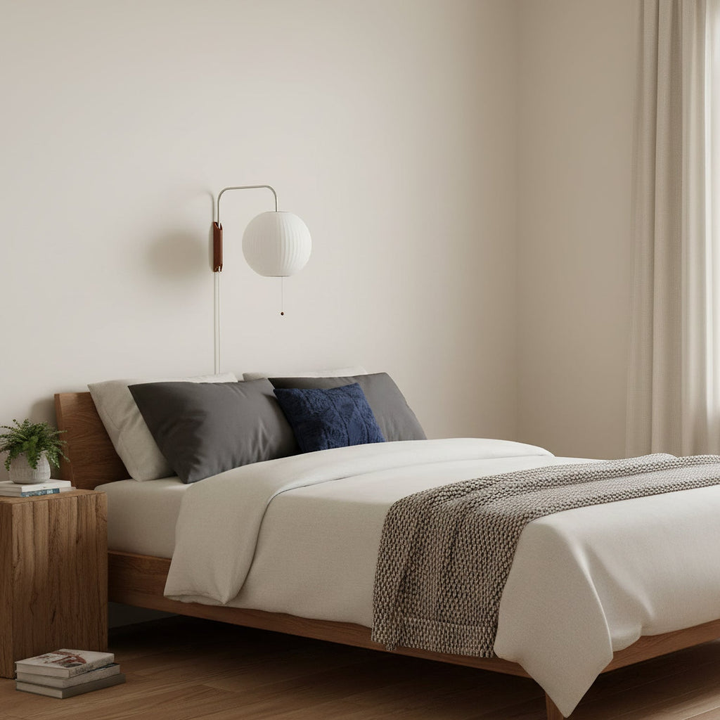 Round white globe on a short curved arm, this Clérachic wall light sits above a walnut bed with grey and navy cushions.