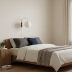 Round white globe on a short curved arm, this Clérachic wall light sits above a walnut bed with grey and navy cushions.