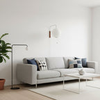 A Clérachic ball-shaped wall light hangs over a grey sofa and white coffee table, with a slim black floor lamp standing beside it.