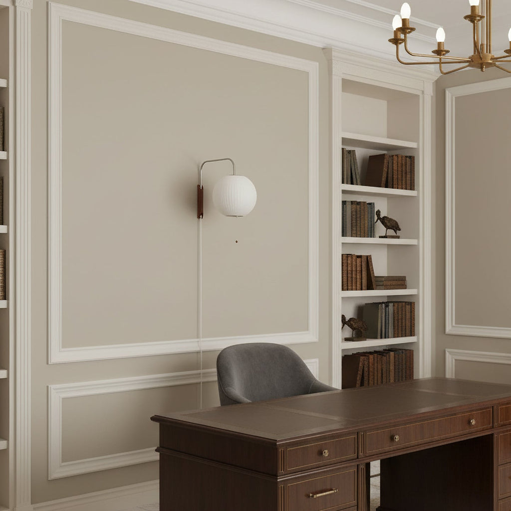 Small round Clérachic wall light on a panelled wall in a study, with built-in shelves, a dark wood desk and a grey chair below.