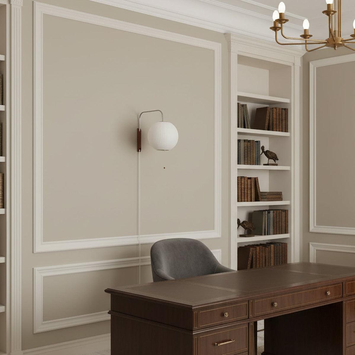Small round Clérachic wall light on a panelled wall in a study, with built-in shelves, a dark wood desk and a grey chair below.