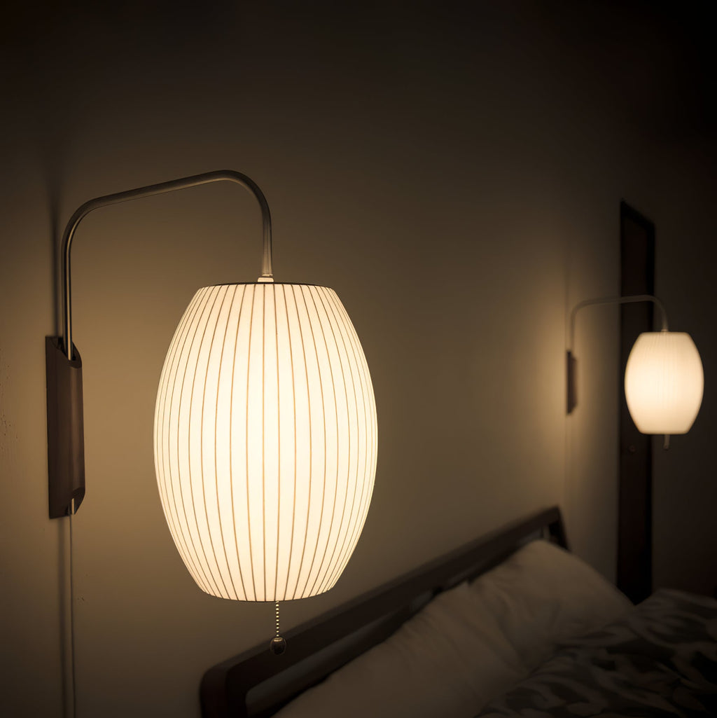Close view of a glowing oval ribbed shade on this Clérachic wall light in a dim bedroom, with a second lit shade behind it.