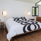 Two Clérachic wall lights with oval white shades sit either side of a low wooden bed dressed in bold black and white bedding.