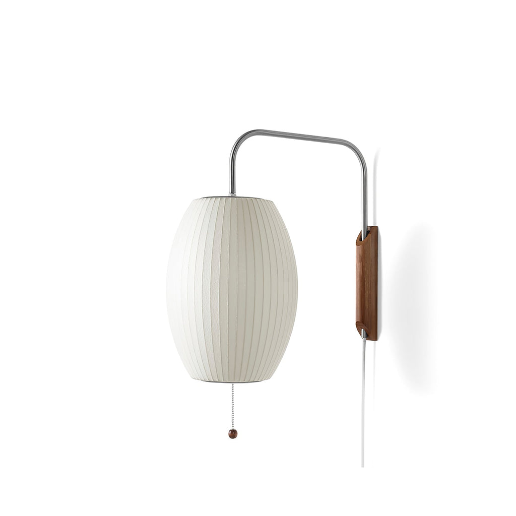 Side view of an oval ribbed shade on a Clérachic wall light, with a steel arm, walnut bracket and pull cord on a white backdrop.