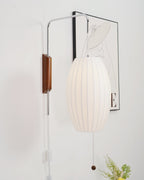Oval white shade of this Clérachic wall light hangs in front of a framed line drawing, with a small vase of yellow flowers at the bottom.