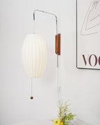 Cropped view of an oval ribbed shade on a Clérachic wall light, its cord and in-line switch running down a white wall beside a framed print.