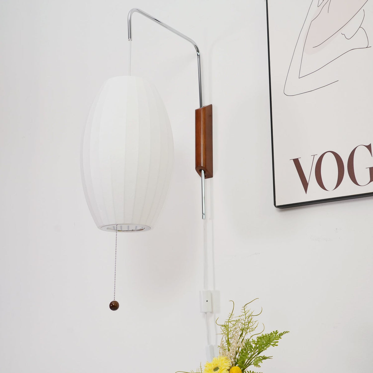 Low-angle view of an unlit oval shade, showing its open base on this Clérachic wall light, with a framed print to the right.