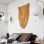 Two round Clérachic wall lights of different sizes flank an ochre woven wall hanging above a daybed where a cat rests.
