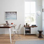 Round white Clérachic wall light by a tall window, above a desk with a laptop, a white chair and a low cabinet.