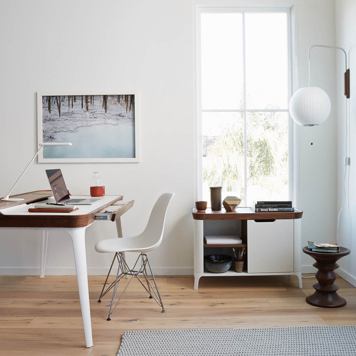Round white Clérachic wall light by a tall window, above a desk with a laptop, a white chair and a low cabinet.