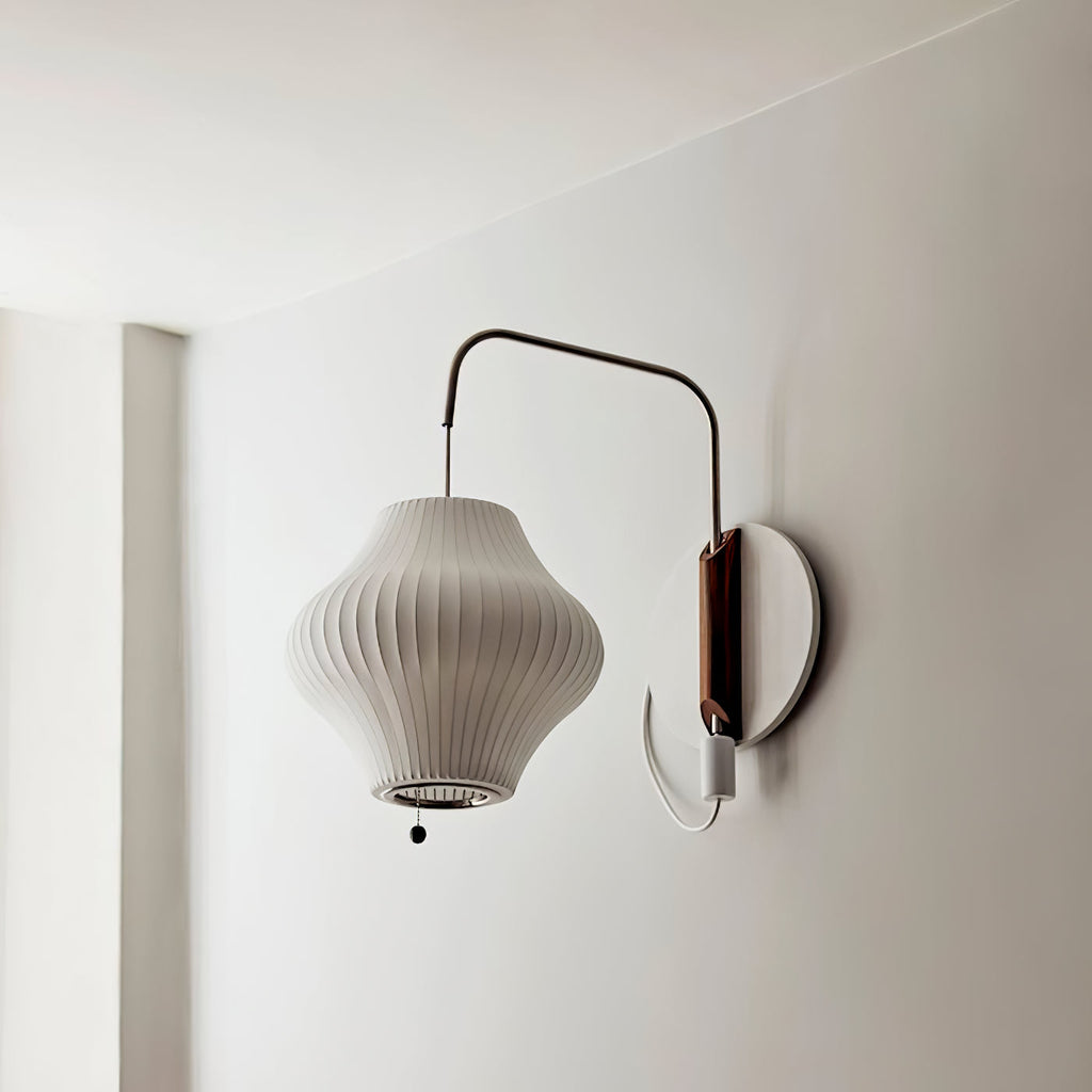 A pear-shaped ribbed shade hangs from a curved arm on this Clérachic wall light, mounted on a round backplate on a pale wall.