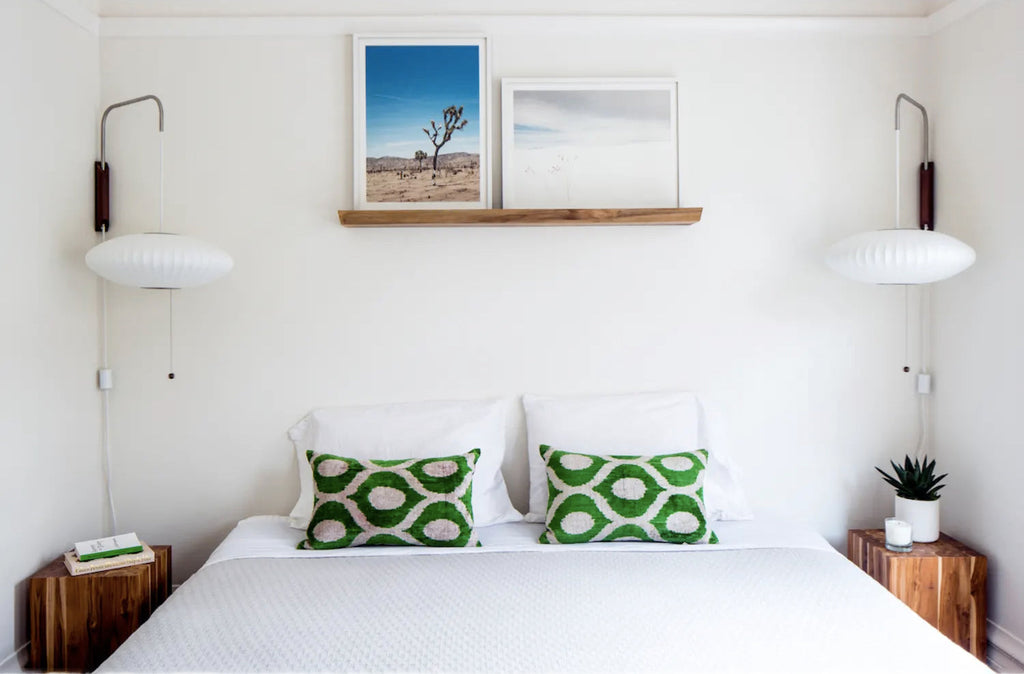 Pair of Clérachic wall lights with flat saucer-shaped shades above a white bed with green patterned cushions and wooden bedside tables.