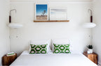 Pair of Clérachic wall lights with flat saucer-shaped shades above a white bed with green patterned cushions and wooden bedside tables.