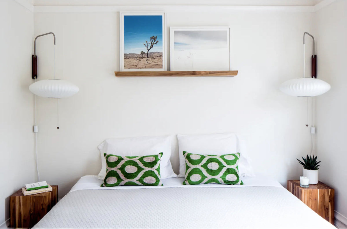 Pair of Clérachic wall lights with flat saucer-shaped shades above a white bed with green patterned cushions and wooden bedside tables.