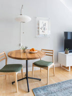Saucer-shaped Clérachic wall light on a white wall above a round wooden table, two chairs with green seats and a small television.