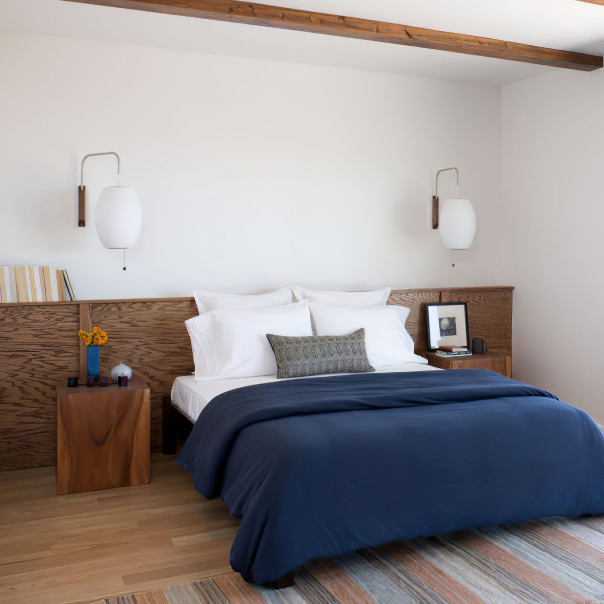 Two oval Clérachic wall lights on either side of a wood-panelled headboard, above a bed with navy bedding and a patterned cushion.
