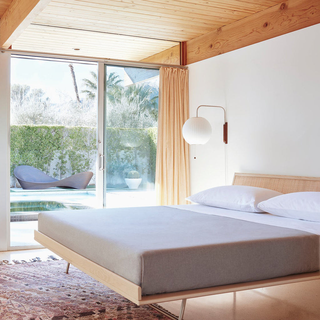 Round white Clérachic wall light beside a sliding door and orange curtain, above a low platform bed and a patterned rug.