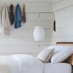 A large oval white shade hangs from a Clérachic wall arm on white boarded panelling, above a bed with white pillows and linen.